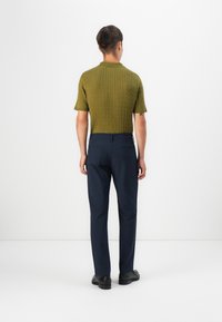 Olivengrøn ribbet strik polo skjorte med korte ærmer, parret med marineblå skræddersyede bukser og sorte sko. Minimalistisk design, glat tekstur.