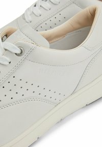 Sneaker in pelle bianca con dettagli perforati, interno beige a contrasto, cuciture tono su tono e lacci bianchi. Design minimalista.