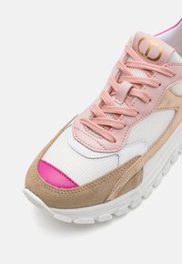 Zapatilla deportiva con parte superior de malla rosa, acentos de cuero blanco, detalles de ante marrón claro y suela blanca gruesa con agarre texturizado.