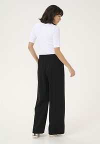 Pantaloni neri a gamba larga con una cintura elasticizzata, abbinati a una maglietta bianca aderente a maniche corte, visti da dietro. Tessuto morbido, stile casual.