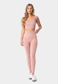 Conjunto atlético de color rosa claro, que incluye una camiseta sin mangas recortada con una textura suave y leggings de cintura alta. Zapatillas blancas complementan el atuendo.