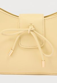 Κοντινή λήψη μιας μπεζ δερμάτινης τσάντας με ραμμένο καπάκι και δέσιμο κορδονιού με χρυσά μεταλλικά άκρα.