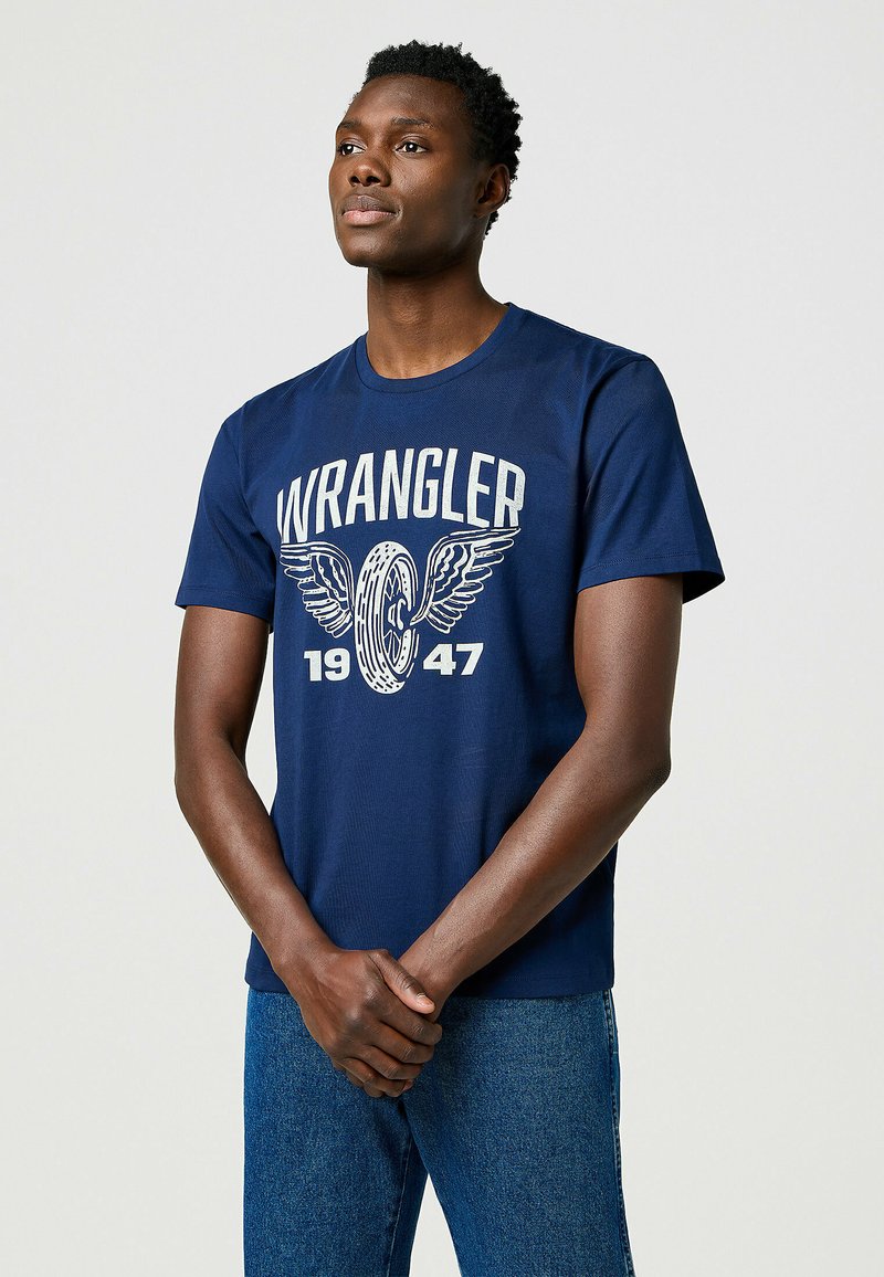 T-shirt blu navy a maniche corte con una stampa grafica bianca raffigurante delle ali, la scritta "WRANGLER" e il testo "1947". Realizzato in cotone.