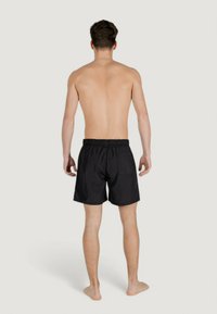 Pantaloni da bagno neri con cintura elastica e tasca laterale. Tessuto morbido, lunghezza sopra il ginocchio, adatti per un abbigliamento da spiaggia casual.