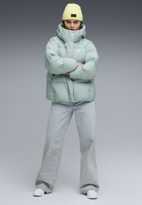 Puffet mintfarvet jakke med høj krave, parret med lyseblå brede bukser og hvide sneakers. Komplementeres med en lys gul beanie.