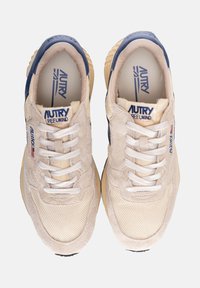 Sneaker sportive beige realizzate in suede e materiale mesh, con punte arrotondate, lacci bianchi e dettagli in blu navy. Marchio ben visibile sulla linguetta.