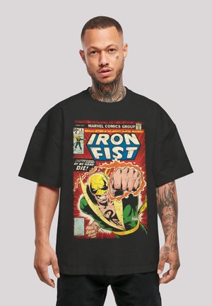 Svart T-skjorte med et Iron Fist-tegneseriekoverdesign med livlige farger, inkludert grønne og gule aksenter, fet tekst og detaljerte illustrasjoner.
