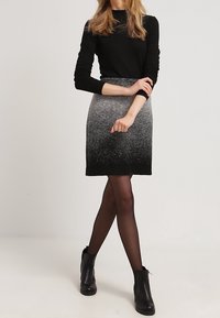 Svart långärmad topp, strukturerad grå ombre kjol som övergår från ljus till mörk, tillsammans med svarta ankelstövlar. Slät tyg, figurnära silhuett.