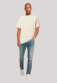 Beige oversized t-shirt, light blue distressed jeans with rips, and white sneakers. Simple design with a relaxed fit and soft texture.