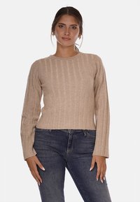 Maglione beige a costine con maniche lunghe e scollatura rotonda, realizzato in un tessuto testurizzato. Indossato con jeans scuri, caratterizzati da un design aderente.