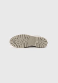 Schuhsohle mit einer strukturierten, gummierten Oberfläche; verfügt über tiefe Rillen und kreisförmige Muster für besseren Grip; überwiegend beige Farbe.