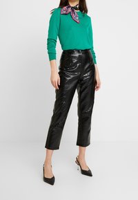 Grön långärmad topp med en mönstrad halsduk, kombinerad med högmidjade svarta byxor i faux-krokodil och svarta spetsiga klackar.