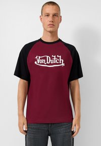 Karmino ir juodos spalvos medvilninis marškinėliai trumpomis rankovėmis, su baltu "Von Dutch" logotipu rašmenimis per krūtinę. Patogus siluetas.