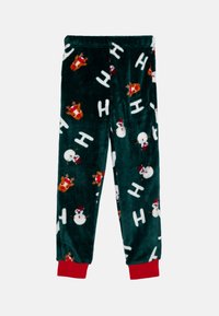 Green plush pajama pants featuring a festive pattern of reindeer and snowmen with red cuffs at the ankle. Dark background, soft texture.