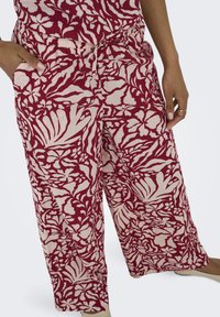 Pantaloni a gamba larga con un motivo floreale rosso e crema. Presentano un elastico in vita e tasche laterali. Realizzati in tessuto leggero.