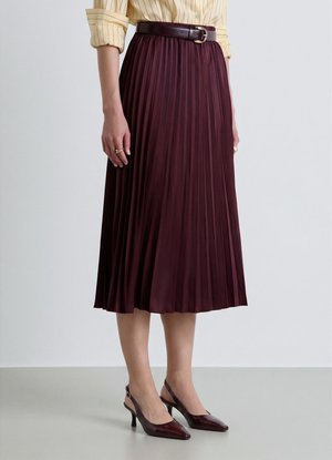 Donna che indossa una gonna midi plissettata con una cintura scura, abbinata a décolleté slingback scuri e a una camicia a righe con le maniche arrotolate.