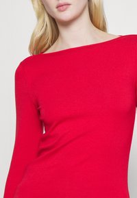 Maglietta rossa a maniche lunghe con design a scollo a barca, silhouette aderente, texture liscia e cuciture minime, caratterizzata da un colore uniforme.