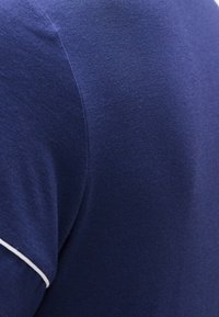 Κοντινό πλάνο υφάσματος σε ναυτικό μπλε, με ραφή και λευκή λεπτομέρεια περιμετρικά της άκρης του μανικιού.