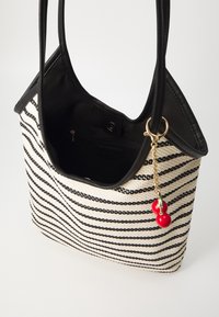 Sac fourre-tout à rayures noires et blanches avec un tissu texturé, une bordure noire lisse, une poche intérieure et un pendentif cerise rouge en accent.