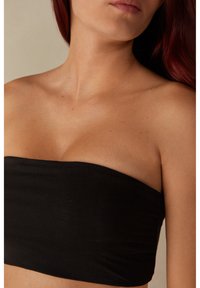 Mustaton, hihnatonta yläosaa, joka on valmistettu sileästä, joustavasta kankaasta. Ominaisuuksiin kuuluu tiivis muotoilu suora kaula-aukko ja ilman näkyviä kiinnikkeitä tai koristeluja.