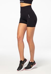 Black high-waisted shorts with fitted design and textured fabric. Worn with black and pink athletic shoes, showcasing a sleek look.