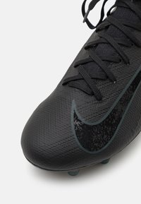 Sort fodboldstøvle med tekstureret overdel, sorte snørebånd og et mørkt mønstret swoosh-design. Udstyret med lys blå studs for godt greb.
