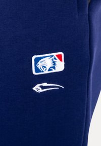 Tela azul marino con logo bordado de una cabeza de gato salvaje rugiente dentro de un rectángulo rojo y azul, y un trazo estilizado blanco debajo.