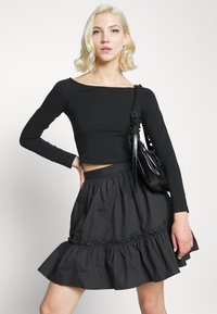 Top cropped preto de mangas longas combinado com uma saia preta com volantes. Apresenta um corpete justo e uma cintura elástica, criando um efeito em camadas.