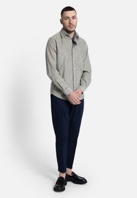 Cămașă cu dungi, cu nasturi, din stofă verde deschis, asortată cu pantaloni negri închis și mocasini negri. Design simplu, formă ajustată.