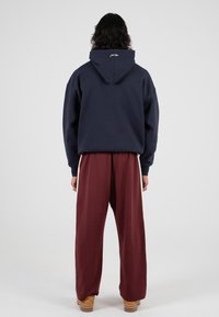 Granatowy hoodie z kapturem o luźnym kroju, zestawiony z luźnymi bordowymi spodniami. Materiał wydaje się miękki o gładkiej fakturze.