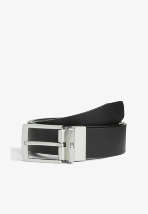 Ceinture en cuir noir roulée avec une boucle en métal argenté et un petit logo rectangulaire rouge, blanc et bleu sur la boucle.