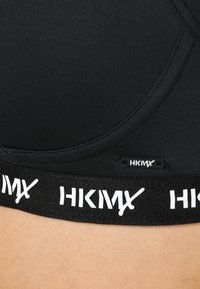 Svart sportsbh med teksturert overflate, buet form og bred elastisk band med hvit "HKMX" merke.