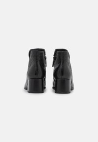 Botas negras de tobillo hechas de cuero con un respaldo texturizado, una punta suave y un tacón tipo bloque. Cuenta con una cremallera lateral para facilitar su uso.
