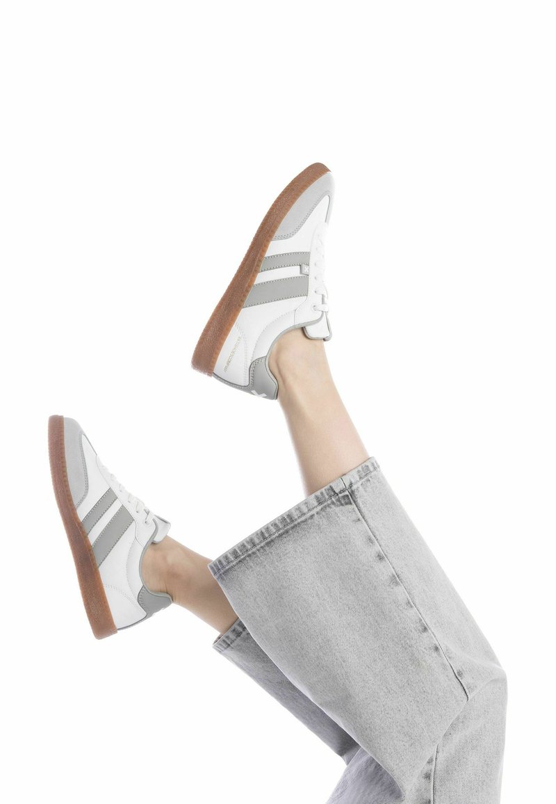 Zapatillas blancas con detalles en gris, de material de cuero, con punta redonda y suela de goma texturizada. Combinadas con unos jeans anchos grises.