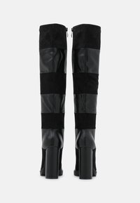 Stivali neri alti fino alla coscia realizzati con una combinazione di materiali lisci e testurizzati, con tacco a blocco e pannelli orizzontali a contrasto.