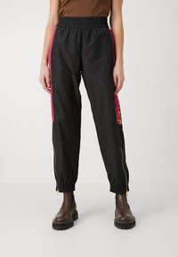 Schwarze Windbreaker-Hosen mit pinken Seitenstreifen, elastischem Bund, Reißverschluss-Taschen und strukturiertem Leoparden-Print-Detail.