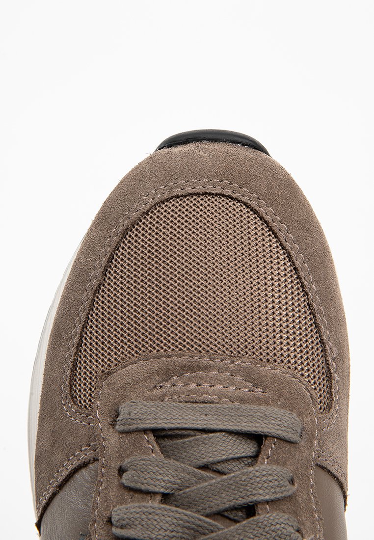 Zapatillas de ante marrón con paneles de malla, punta redonda y cordones planos. Cuenta con un acento negro en la punta y detalles de tejido texturizado.