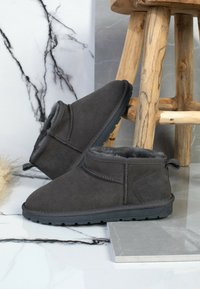 Botas de tobillo de ante gris con un forro suave, puntera redonda y suela de goma, con un lazo trasero para facilitar el calzado.