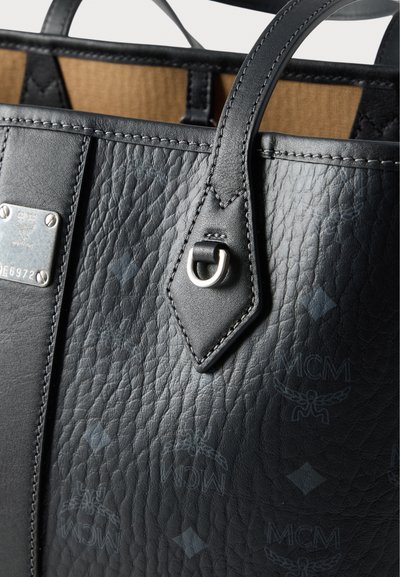 Μαύρη τσάντα tote από δέρμα με υφή, με μεταλλικά εξαρτήματα, διακριτικά ανάγλυφα σχέδια και λείο εσωτερικό επένδυση.