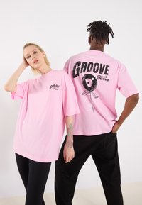 Pink oversized t-shirts with short sleeves. Front features "GROOVE" logo; back includes a design of a record with musical notes.