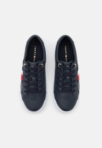 Sneaker in pelle di colore navy con suola in gomma bianca, dotate di lacci neri, dettagli in metallo dorato e un logo rosso e bianco sul lato.