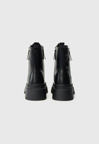 Czarne skórzane botki na kostkę z masywną podeszwą, bocznymi suwakami i pętelkami z tyłu. Gładka faktura z delikatnymi przeszyciami.