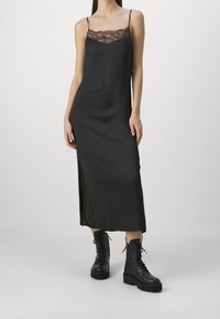 Robe noire sans manches avec une bordure en dentelle au niveau du col, dotée de fines bretelles et d'une fente sur le côté, associée à des bottes de combat noires à lacets.