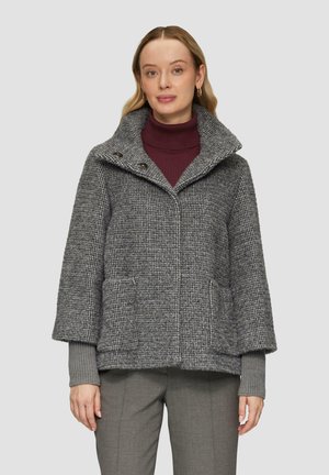 Manteau en tissu texturé gris avec un grand col, deux poches avant et une fermeture à boutons, porté sur un col roulé bordeaux.