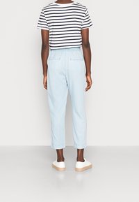 T-shirt rayé à manches courtes, blanc et bleu marine, associé à un pantalon bleu clair à taille élastique, et des chaussures blanches à semelle plateforme en jute.