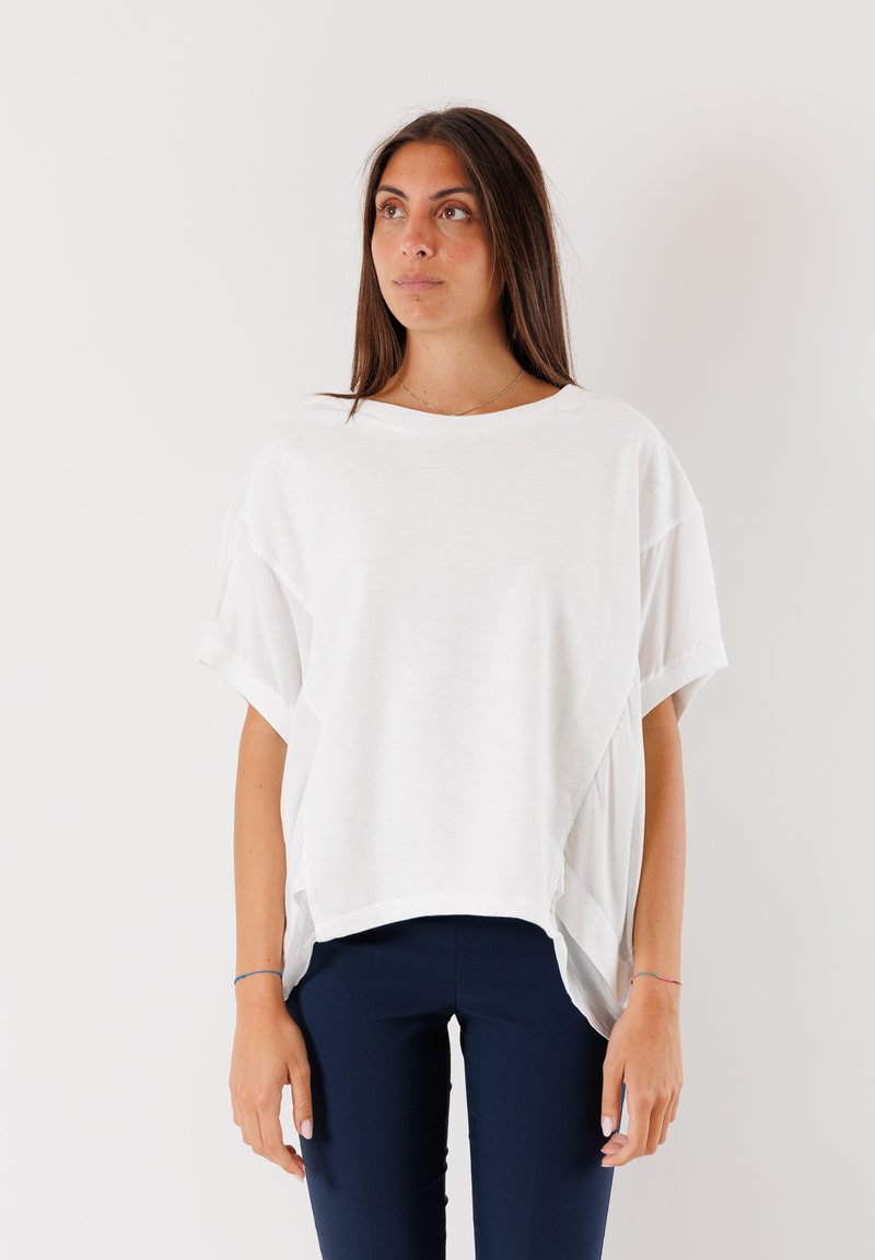 Top bianco a maniche corte con una vestibilità rilassata, design a strati e scollatura rotonda. Abbinato a pantaloni aderenti blu scuro. Tessuto liscio.