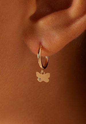 Boucle d'oreille en or avec un charme en forme de papillon et une seule pierre précieuse transparente. Gros plan de la boucle d'oreille portée à une oreille.
