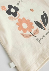 Tejido de color beige claro con un diseño floral. Incluye flores en negro, naranja y blanco con hojas verdes. El texto dice "¡floréame!"