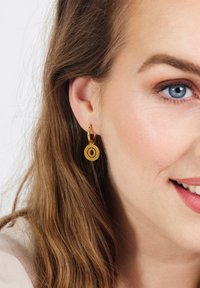 Gouden hoop oorbellen met een ronde hanger, met een open cirkelontwerp. De oorbellen zijn glanzend en complementeren de gladde haartextuur.