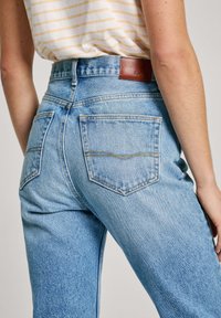 Vaqueros de denim azul claro con una cintura alta y corte recto, que cuentan con bolsillos traseros y una marca de cuero marrón en la cinturilla.